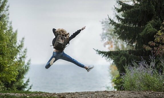 zdjęcie przedstawiające skaczącą wysoko dziewczynę z plecakiem w tle zarys gór